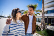 © CarlosBarquero - Young couple walk closely together and look at each other in a sunny residential neighborhood with modern architecture and a relaxed travel atmosphere.