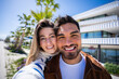 © CarlosBarquero - Young man and woman pose closely and smile at camera outdoors in a sunny modern neighborhood, creating a warm lifestyle and relationship portrait.