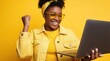 © miss irine - Happy young Black woman celebrates success looking at laptop screen. Excited girl wearing yellow glasses, denim jacket cheers in front of bright yellow background. Joyful female student wins online