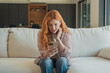 © Daniel - Young woman reacts with happy surprise while holding a smartphone on a sofa at home. Her wide-eyed response captures mobile communication, social media, exciting news, and daily technology use.