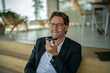 © BusinessClass by W61 - Smiling businessman records a voice message on his smartphone indoors