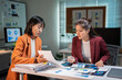 © MINAE - Businesswomen collaborating on data analysis, reviewing reports, discussing strategy late at night in a modern office