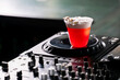 © pavel siamionov - Red cocktail with thick foam and chocolate garnish sitting on a DJ mixer platter in a dimly lit club setting.