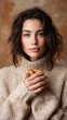 © Irina - Young brunette woman in a cozy beige sweater holds a sesame pretzel and looks at the camera against a warm neutral background.