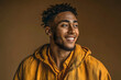 © Audrey - Smiling young man in a casual yellow outfit against a khaki background conveying a cheerful and stylish expression
