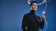 © f_bossa - Man in black turtleneck holds a glowing fiber optic strand against a dark blue background. Bright orange luminescence trails through the air in swirling loops around his head.