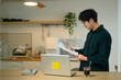 © Prathankarnpap - Young Man Reading Document While Working From Home at Kitchen Counter