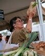 © Ryzhkov - Senior woman holding a squash at an outdoor market, thoughtful expression with earthy vegetables for healthy living and wellness