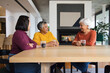 © WavebreakMediaMicro - Diverse female friends sitting and chatting at dining table holding glass mugs by fireplace