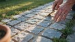 © SHAHIN - Close up of worker hands carefully sweeping sand into gaps of newly laid stone pavers for garden pathway.