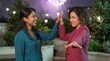 © boztaga - Two young women exchange a playful high five in a lush outdoor terrace setting while fireworks glow overhead, expressing friendship, confidence, and upbeat excitement at a midnight celebration