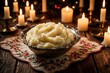 © miss irine - Creamy mashed potatoes in silver bowl on rustic wooden table. Lit candles, floral placemat create cozy festive atmosphere. Warm homemade side dish with delicious texture for holiday dinner