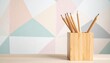 © Nuii Digital Art - Natural wooden pencil holder filled with sharpened pencils on a desk against a soft pastel geometric wall, creating a minimalist workspace with copy space for education, school, and creative projects