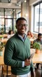 © Mono - A smiling young Black man wearing glasses and a green sweater, holding a tablet in a modern co-working office.