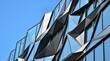 © PARUL - Low angle view of a building facade with geometric glass windows and dark metal triangular panels reflecting the clear blue sky in daylight