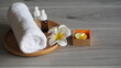 © kanjana - Relaxing spa and wellness setting with a rolled white towel, aromatherapy essential oil bottles, fresh frangipani flowers, and a glowing candle arranged on a wooden tray. The peaceful natural composit