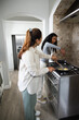 © WavebreakMediaMicro - Female friends cooking at stove, stirring eggs with wooden spatula on freestanding gas range