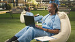 © DC Studio - Medical student in blue scrubs types on a laptop with a stethoscope while taking notes and studying on a beanbag in a campus healthcare setting.