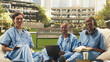 © DC Studio - Diverse medical students smile while seated on grass during group study, using stacked books, a laptop and coursework notes for healthcare learning.
