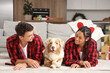 © Pixel-Shot - Holiday family bonding and pet care, happy couple with Australian shepherd dog lying on floor at home during Christmas season with festive decor