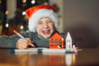 © Westend61 - Smiling boy in Santa hat writing a Christmas letter indoors