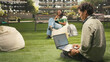 © DC Studio - International student uses a laptop with coding content on a campus bench while classmates study in the background for outdoor learning; IT automation study continues in an academic environment.