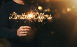 © velikiyzayats - Man holding sparkler forming the text Limited Offers celebrating a special discount and promotion event in the dark