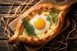 © Maryna - Top view of traditional Georgian khachapuri adjara. Boat shaped bread filled with melted cheese, runny egg yolk. Fresh dill garnish on tasty cheese pie. Homemade ethnic cuisine served on wooden board