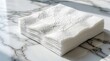 © Lubov - Stack of clean white paper napkins on marble tabletop. Pile of disposable napkins with textured pattern sits on luxury stone surface. Tableware for dining in restaurant kitchen, cafe home decor.