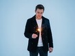 © faisal - A handsome caucasian male stands outdoors in a winter setting holding a glowing sparkler. The man wears a stylish black coat over a white sweater, gazing peacefully at the bright festive