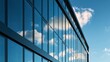 © Tina - Modern glass building facade with reflective windows against a bright blue sky with white clouds. The geometric grid pattern and sleek architecture create a contemporary urban aesthetic.