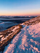 © Travel 'n' Lifestyle - View of a snow-covered mountain path during golden hour with rocky terrain, distant peaks, and a layer of mist in the valley in the United Kingdom.