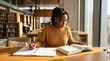 © Evandro - Black college student studying quietly in a modern library with books and notebook