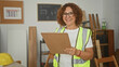 © Krakenimages.com - Woman carpenter holding clipboard and smiling while reading in building; safety inspection confidence.