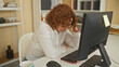 © Krakenimages.com - Woman in white shirt and glasses typing at computer with hand on chin while leaning forward at desk in building office; fatigue focus.