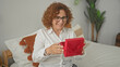 © Krakenimages.com - Woman with curly hair and glasses smiling while opening red gift box on bed in building; surprise joy.
