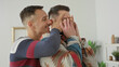 © Krakenimages.com - Two men in casual sweaters hug as one covers the other's eyes with hands while smiling and playfully surprising him in a building; playful intimacy.