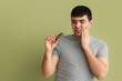 © Pixel-Shot - Toothache and dental pain, man holding chocolate bar with sensitive teeth and oral health problem on a solid green background
