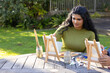 © Wavebreak Media - Indian woman sitting at wood table in garden, painting on easel with palette wearing green sweater