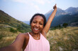 © CarlosBarquero - A Latina African American woman smiles and raises an arm above her head while taking a selfie in a mountain valley. Photographed in the Aiguestortes area of the Spanish Pyrenees.