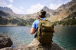© CarlosBarquero - A Caucasian man stands facing the lake and surrounding rocky peaks, wearing a green backpack and hiking hat. Photographed in the Aiguestortes area of the Spanish Pyrenees.