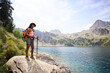 © CarlosBarquero - A Latina African American woman stands on a large rock with trekking poles and a yellow backpack beside an alpine lake. Photographed in the Aiguestortes area of the Spanish Pyrenees.