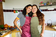 © Alvaro Lavin/Stocksy - Women smiling posing in kitchen wearing aprons