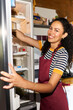 © Alvaro Lavin/Stocksy - Smiling woman reaching inside refrigerator in kitchen