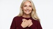 © Vadym - Smiling mature blonde woman puts hands on chest with gratitude. Happy senior lady feels emotional, thankful in studio. Elegant female person wears maroon sweater, shows positive feeling. Beautiful