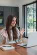 © Daniel - Woman greets colleagues with raised hands during a team meeting on her laptop at home. Her smile and open gesture support remote work, workplace communication, collaboration and online connection.