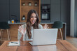 © Daniel - Woman celebrates good news with raised hands during a video call on her laptop at the kitchen table. Her excited reaction suits an online announcement, virtual celebration and positive communication.