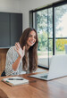 © Daniel - Woman welcomes classmates with a wave during an online class on her laptop at home. Her smile supports distance learning, virtual education, student participation, digital communication and study.