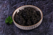 © Andrei Starostin - Ceramic bowl holding black caviar garnished with fresh green parsley on textured dark surface gourmet seafood delicacy