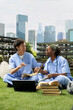 © DC Studio - Medical students in scrubs exchange ideas over notebooks, stacked textbooks and a laptop while studying together on the campus lawn, using peer discussion to prepare for healthcare training.